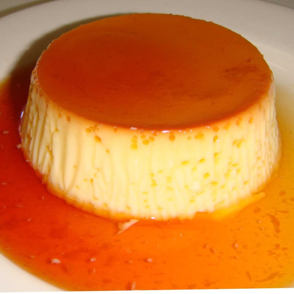Caramel flan with a smooth custard center sits on a white plate surrounded by glossy caramel sauce.