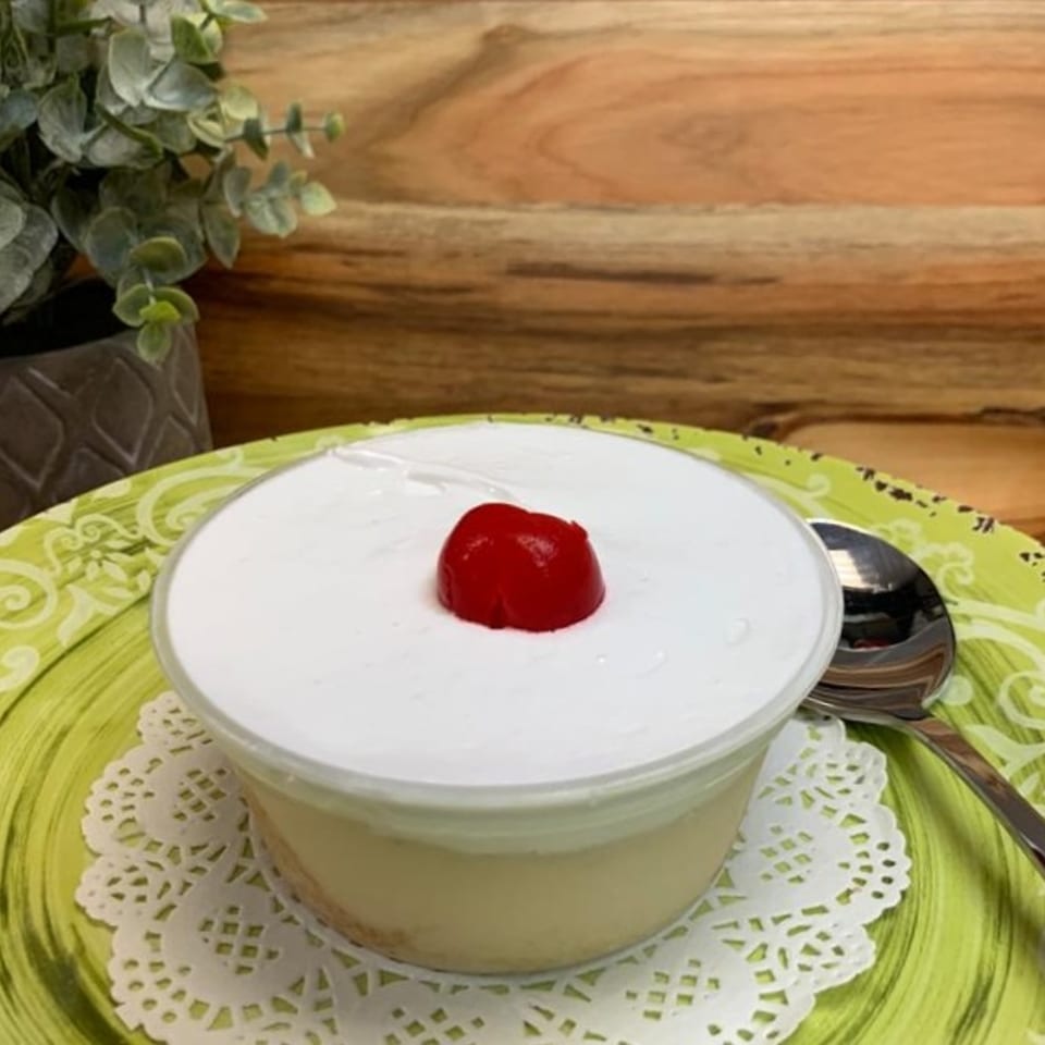 Creamy dessert topped with a red cherry, served in a glass bowl on a green patterned plate with a spoon.