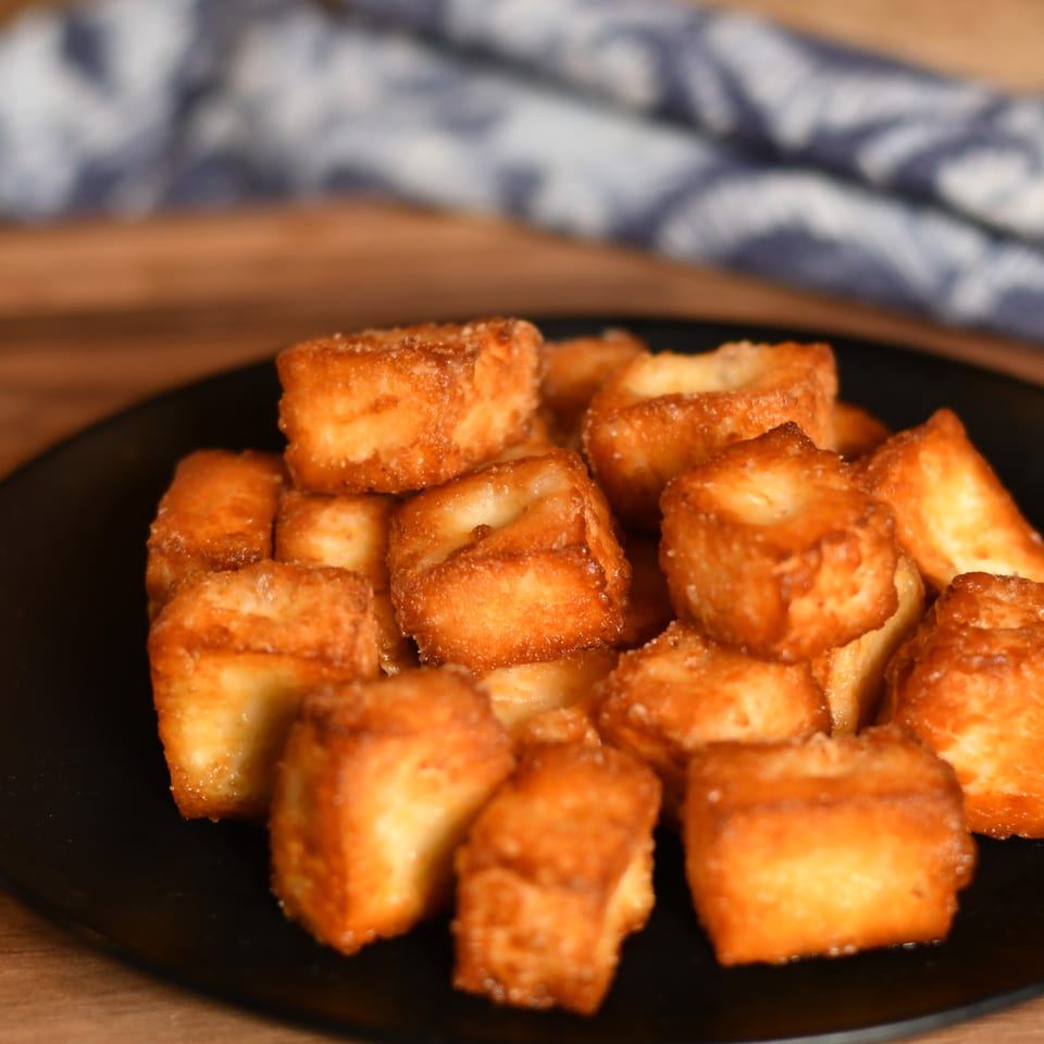Golden-brown fried cheese bites piled on a black plate atop a wooden table.